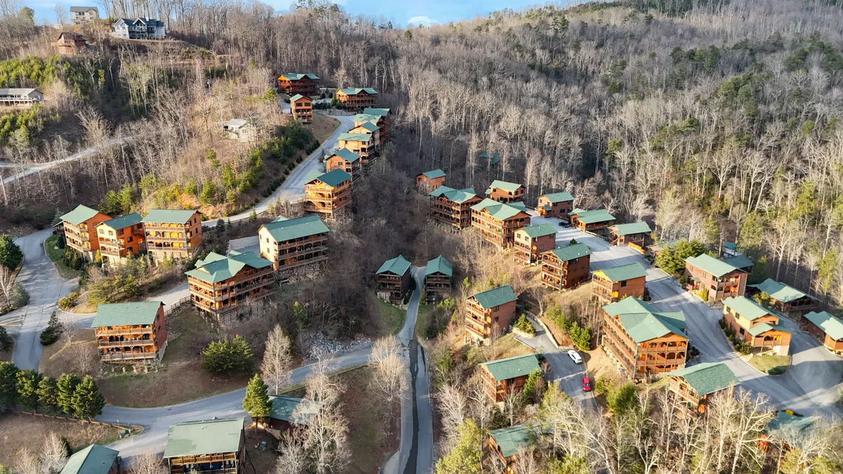 A charming exterior view of a cluster of cabins nestled among trees, connected by winding roads and surrounded by lush greenery, invoking a sense of togetherness and exploration in a natural setting.