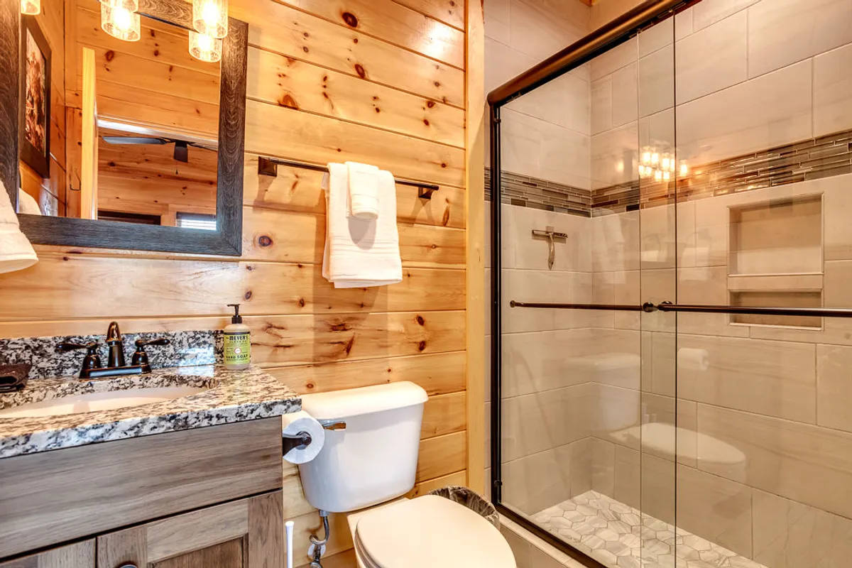 A modern bathroom with a granite countertop, stylish glass shower enclosure, and wooden accents. The ample space and serene décor highlight an inviting atmosphere for refreshing morning or evening routines.