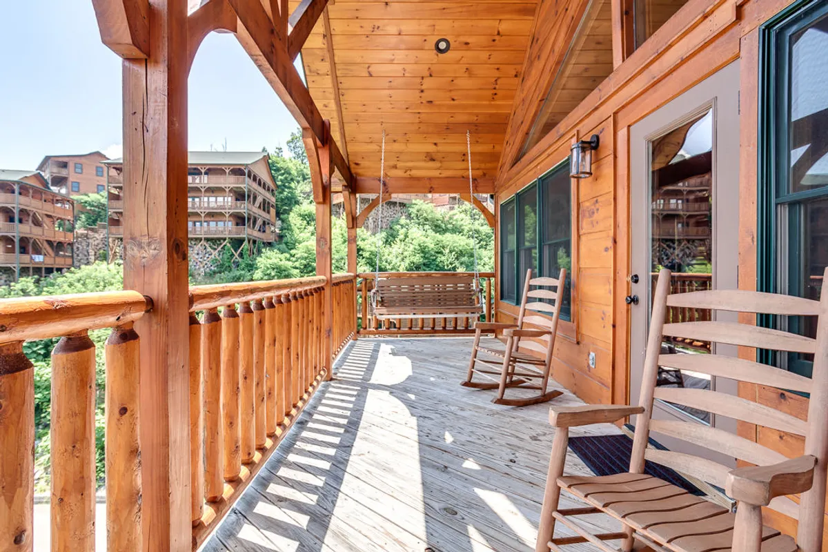Featuring a spacious wooden porch with rocking chairs, a swing, and lush greenery all around, this image captures the tranquil transition between indoor comfort and the wild, inviting outdoors. The scene invites guests to relax, socialize, or simply soak in the natural surroundings after a day of adventure.
