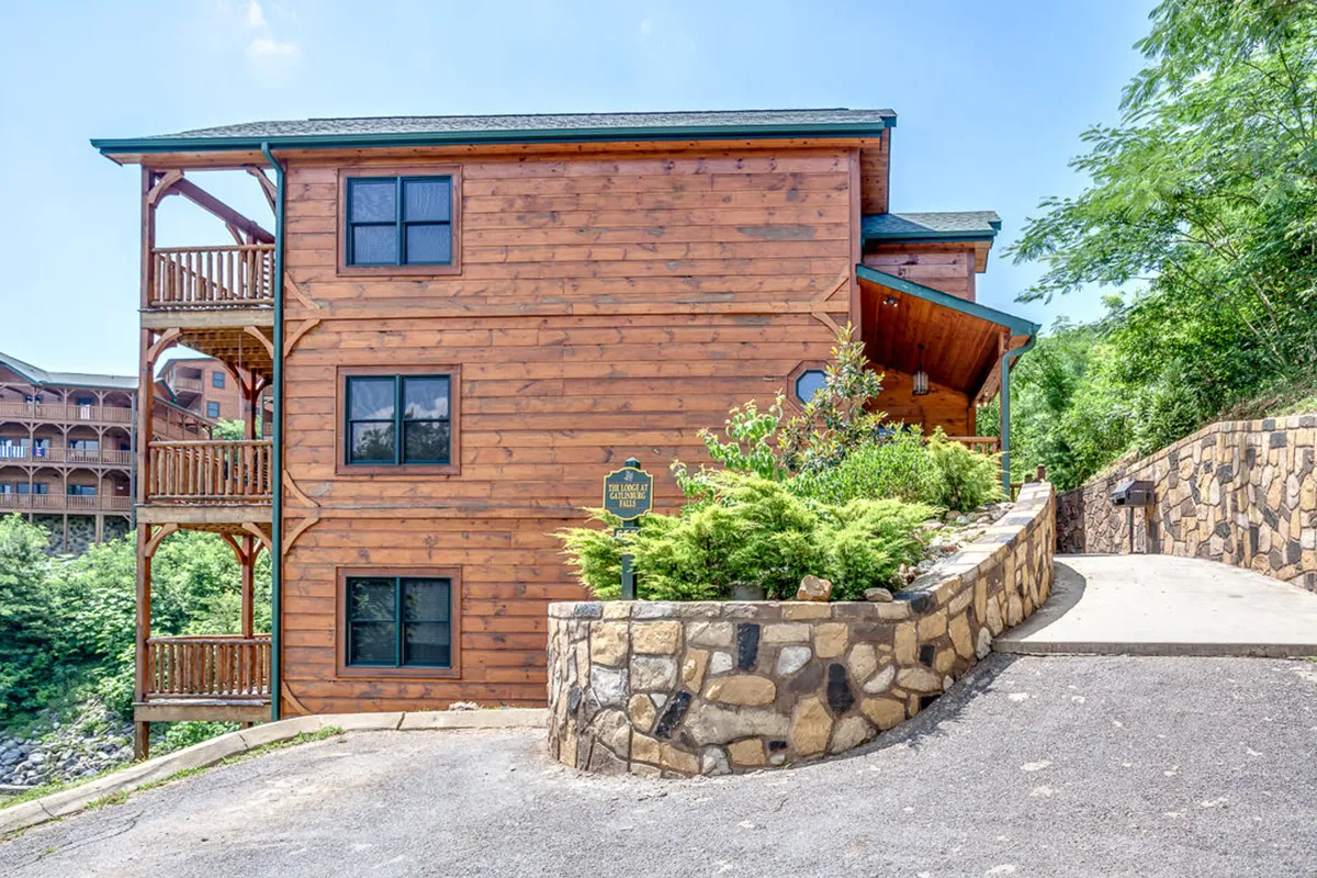 The exterior of the cabin with multiple balconies overlooking landscaped gardens and lush surroundings. The balconies are furnished, offering spots for morning coffee or evening BBQs against a backdrop of mountain views.
