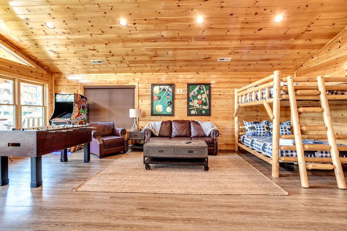 A lively interior shot of a game room featuring bunk beds, leather sofas, a foosball table, and an arcade game—inviting spaces for group play, relaxation, and shared fun.