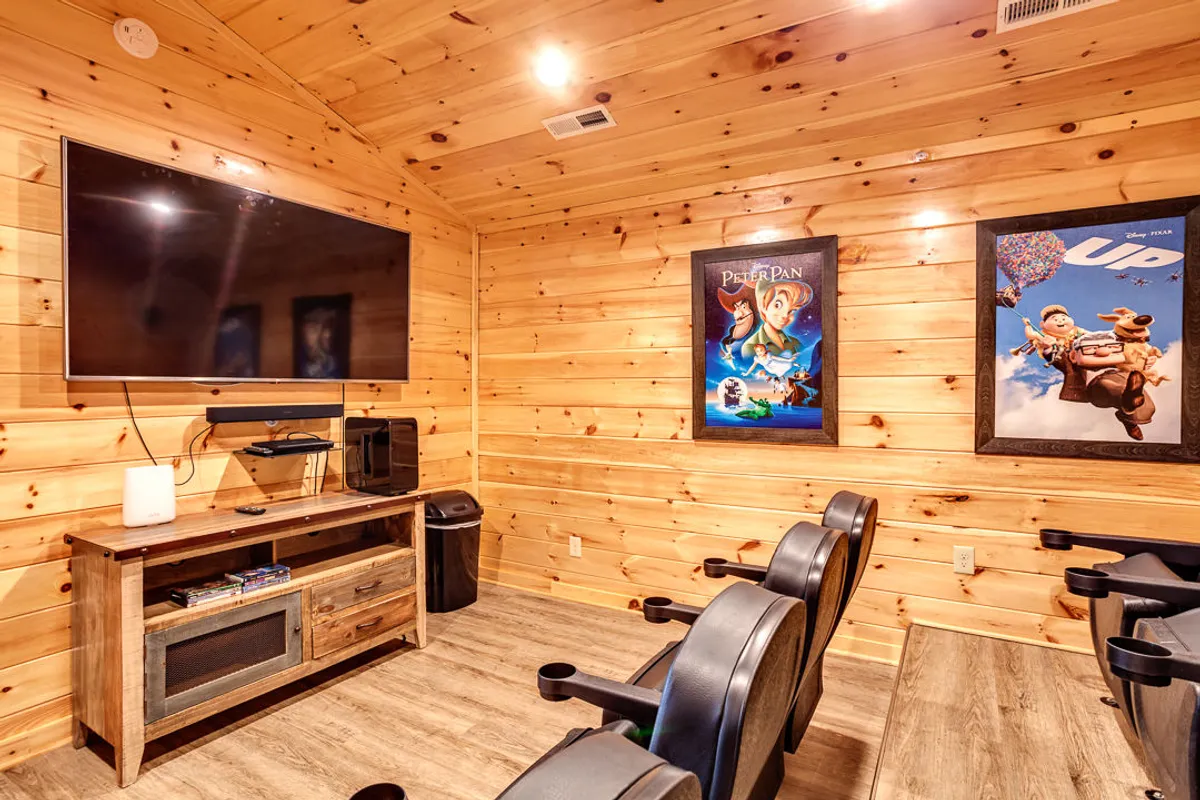 This cozy theater room features a large television, a wooden entertainment unit, and movie posters. The seating area is designed for comfort, ideal for hosting movie nights with family or friends after a day spent outdoors.