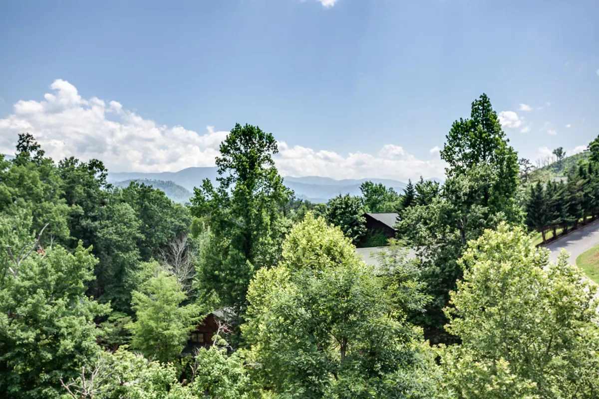 A sweeping view of lush greenery, distant blue mountains, and a bright sky, capturing the grandeur of the Smoky Mountains. The scenery evokes a sense of peacefulness and adventure, inviting guests to explore the natural wonders just beyond the doorstep.