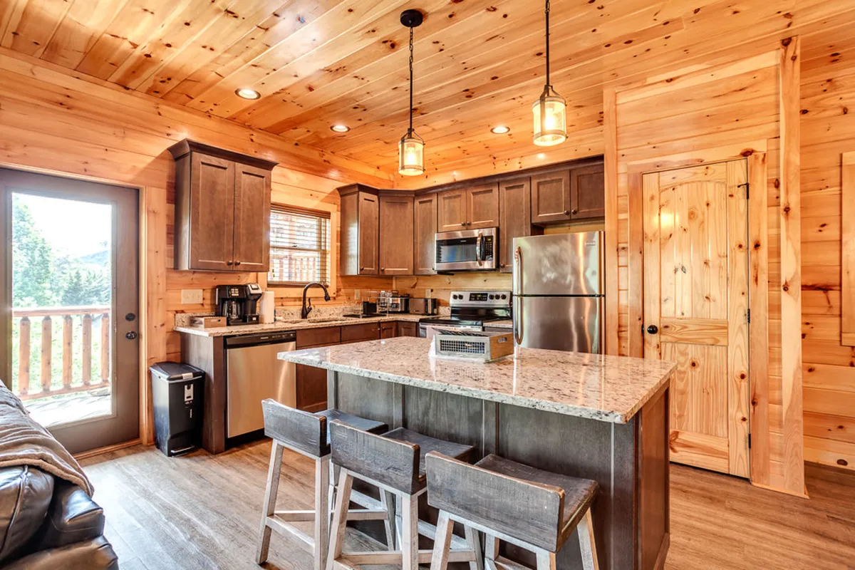 A bright, welcoming kitchen with granite countertops, wood cabinetry, pendant lighting, bar stools, and a large window overlooking the outdoors—inviting families to cook, socialize, and share meals together.