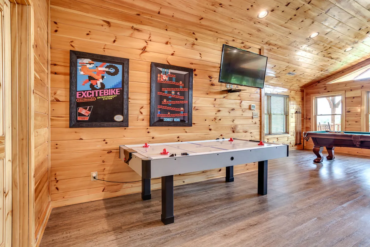 A lively game room view featuring an air hockey table, vintage game posters, television, and a pool table. The space is inviting for both adults and children, set up for friendly competitions and group celebrations.